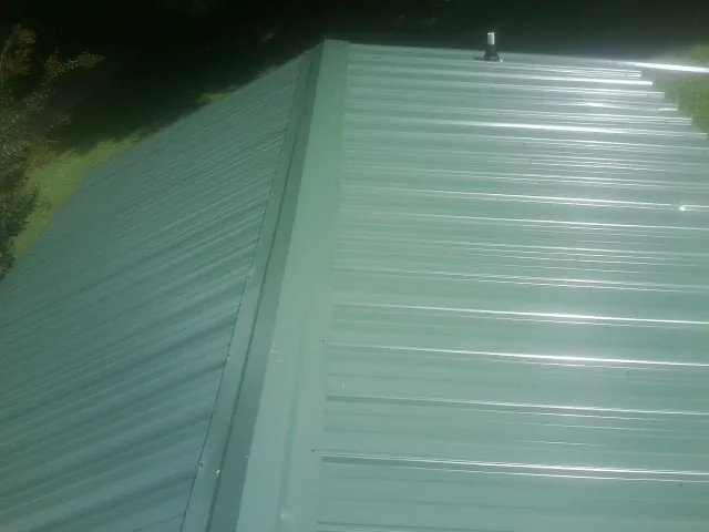 New green metal panels meeting at the ridge of a roof — Flat Roof Repair work by our crew in Claremont